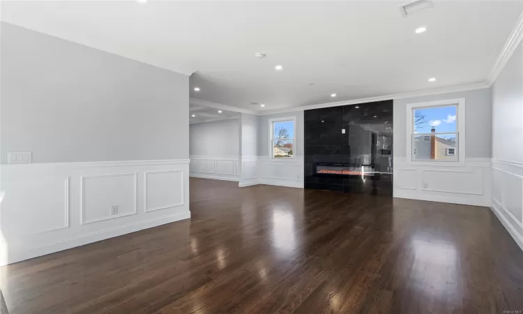 Unfurnished living room with dark hardwood / wood-style floors, ornamental molding, a wealth of natural light, and a premium fireplace