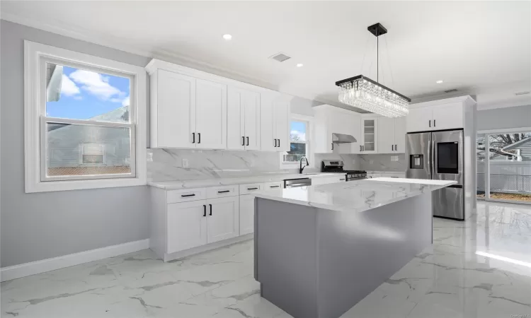 Kitchen with stainless steel appliances, a kitchen island, backsplash, decorative light fixtures, and white cabinets