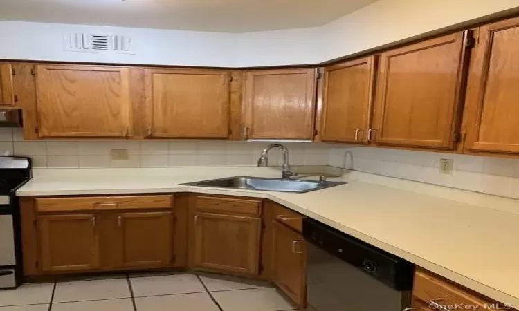 Kitchen with dishwasher, stove, light tile patterned floors, and sink