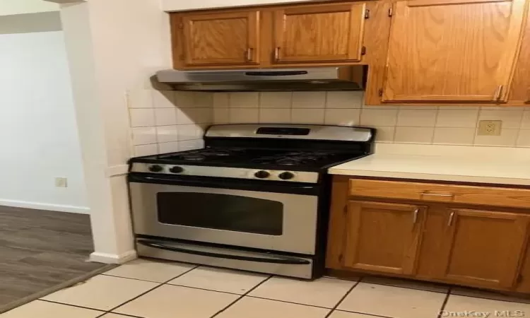 Kitchen featuring light tile patterned floors, backsplash, ventilation hood, and stainless steel range with gas cooktop