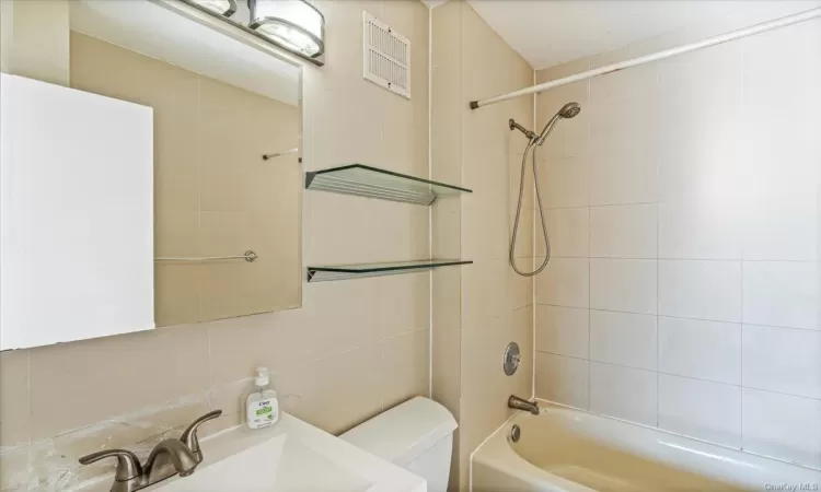 Full bathroom with toilet, tile walls, sink, and tiled shower / bath