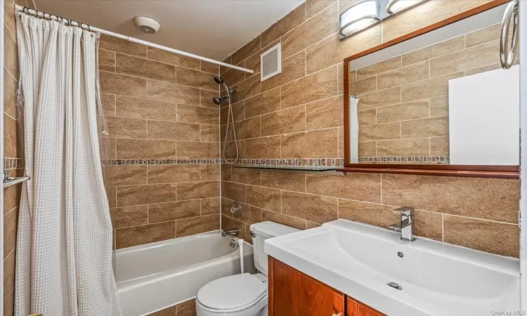 Full bathroom with shower / bath combo, tasteful backsplash, toilet, vanity, and tile walls