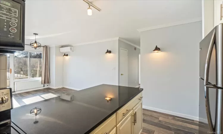 Kitchen with stainless steel refrigerator, dark hardwood / wood-style flooring, a wall mounted AC, cream cabinetry, and ornamental molding