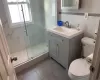 Bathroom featuring an enclosed shower, vanity, toilet, and tile walls