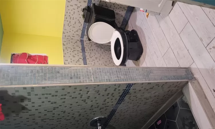 Bathroom featuring tiled shower, hardwood / wood-style floors, tile walls, and toilet