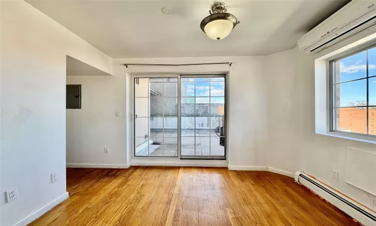 Spare room featuring baseboard heating, electric panel, light wood-type flooring, and an AC wall unit