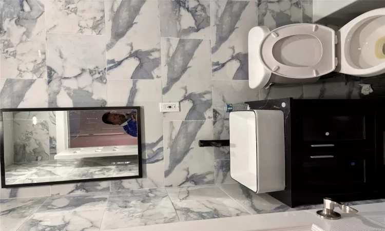 Bathroom featuring vanity, tile walls, and toilet