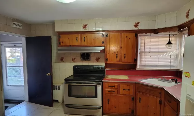 Kitchen with sink, light tile patterned floors, radiator heating unit, hanging light fixtures, and stainless steel range with electric cooktop