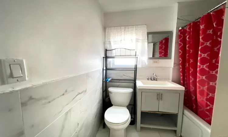 Full bathroom with tile patterned floors, toilet, shower / bath combo with shower curtain, vanity, and tile walls