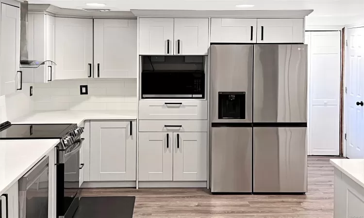 Kitchen with white cabinets, backsplash, light and stainless steel appliances