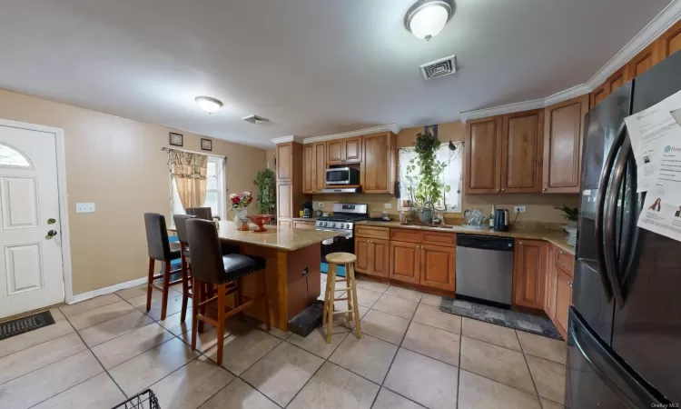 Kitchen featuring light stone countertops, a center island, stainless steel appliances, a kitchen bar, and light tile patterned flooring