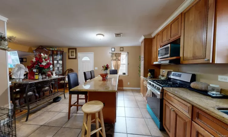 Kitchen with light stone countertops, a breakfast bar, stainless steel appliances, light tile patterned floors, and a center island