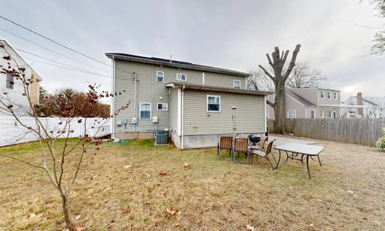 Rear view of property featuring central air condition unit and a lawn