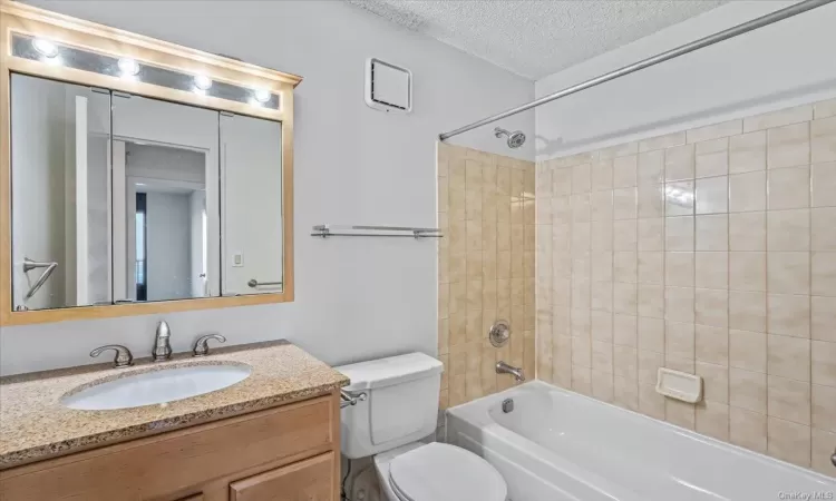 Full bathroom featuring tiled shower / bath combo, toilet, a textured ceiling, and vanity