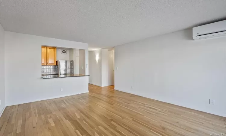 Unfurnished living room with a wall unit AC, light hardwood / wood-style flooring, and a textured ceiling