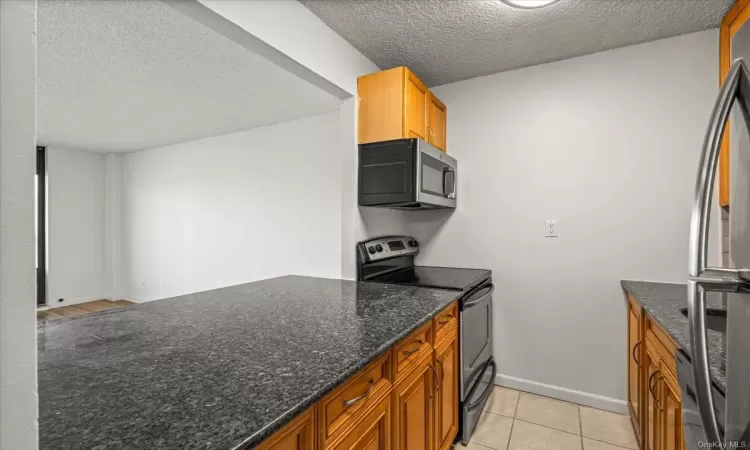 Kitchen with dark stone countertops, light tile patterned floors, a textured ceiling, and appliances with stainless steel finishes