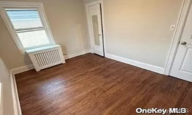 Unfurnished room featuring dark hardwood / wood-style flooring and radiator heating unit