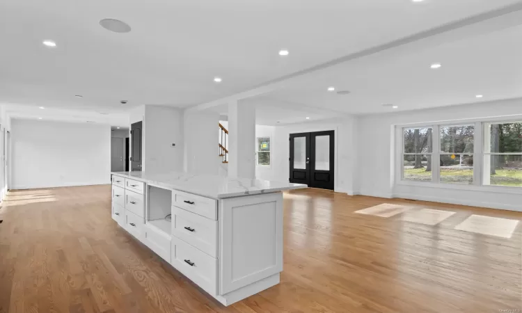 Kitchen featuring light stone countertops, a center island, french doors, white cabinets, and light wood-type flooring