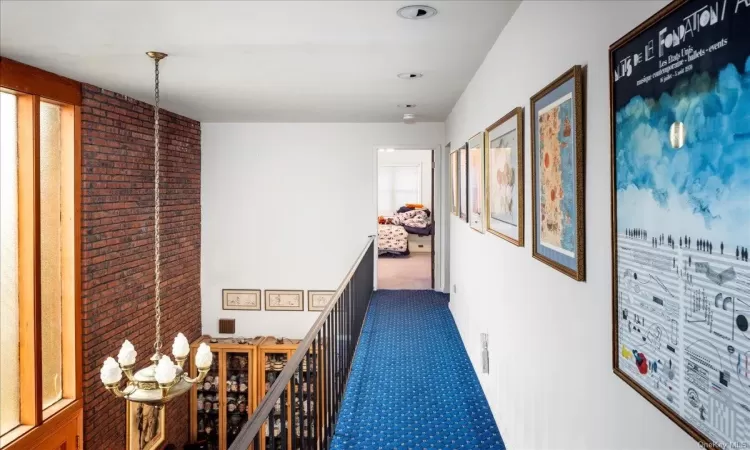 Hall featuring dark carpet, brick wall, and an inviting chandelier