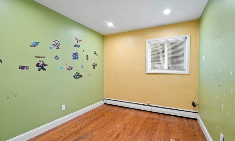 Empty room featuring wood-type flooring and a baseboard radiator