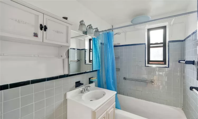 Bathroom featuring shower / bath combination with curtain, vanity, and tile walls