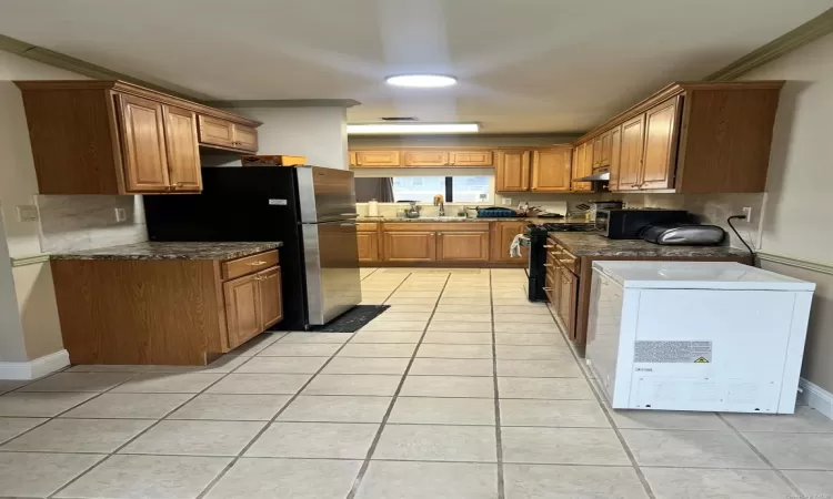 Kitchen with black range oven, light tile patterned floors, crown molding, and tasteful backsplash