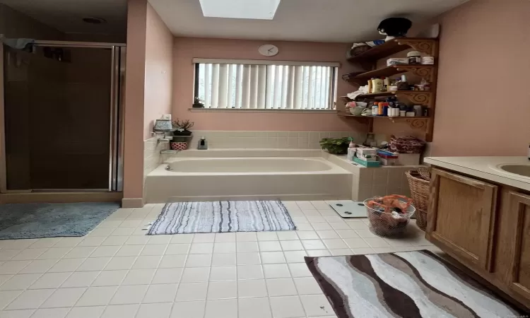 Bathroom with plus walk in shower, vanity, a skylight, and tile patterned floors