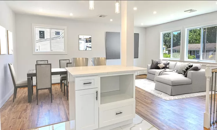 Kitchen with a center island, white cabinets, decorative light fixtures, light hardwood / wood-style floors, and light stone counters