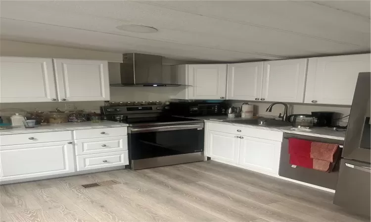 Kitchen featuring range hood, white cabinetry, light hardwood / wood-style flooring, and stainless steel range oven