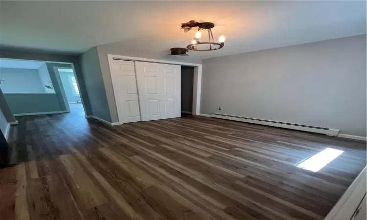 Unfurnished bedroom featuring a baseboard heating unit, a chandelier, dark hardwood / wood-style floors, and a closet