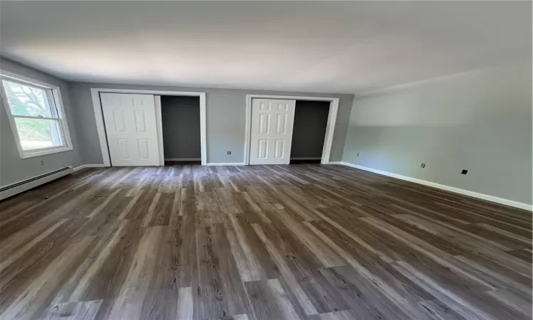 Unfurnished bedroom featuring baseboard heating, two closets, and dark hardwood / wood-style floors