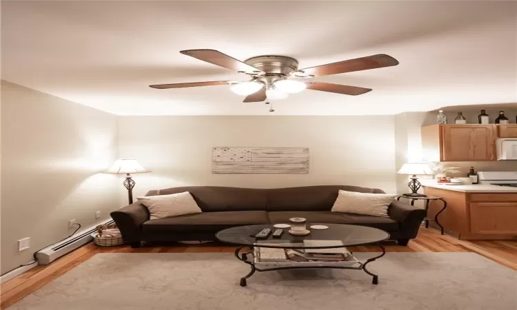 Living room with ceiling fan, a baseboard heating unit, and light wood-type flooring