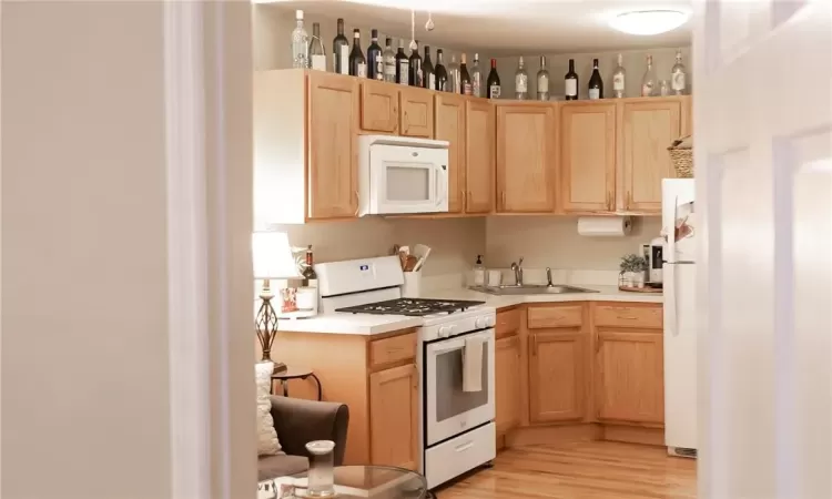 Kitchen featuring light hardwood / wood-style flooring, sink, light brown cabinetry, and white appliances