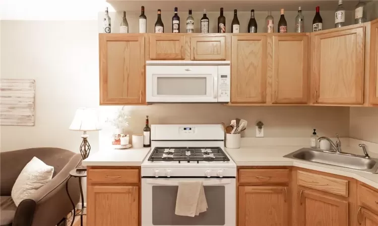 Kitchen featuring light brown cabinetry, sink, and white appliances