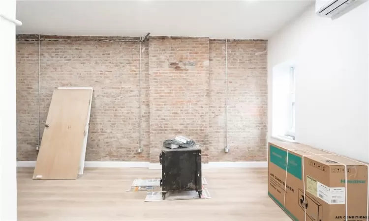 Empty room with brick wall, a wall mounted AC, and light wood-type flooring