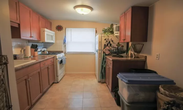 Kitchen featuring sink, tasteful backsplash, white appliances, and light tile floors