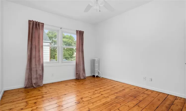 Empty room featuring ceiling fan, radiator, and light hardwood / wood-style flooring