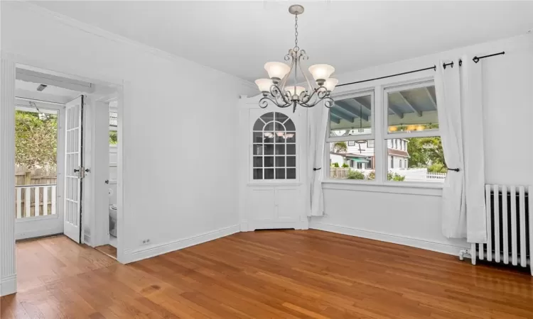 Unfurnished dining area with ornamental molding, a notable chandelier, radiator, and hardwood / wood-style floors