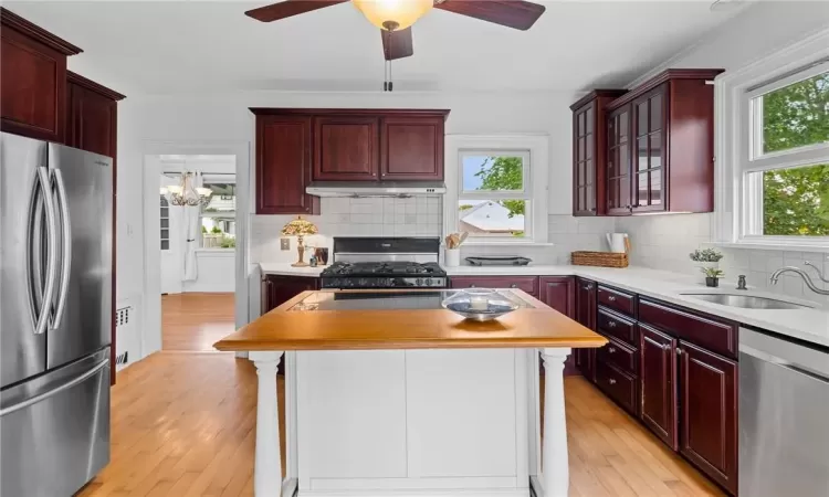 Kitchen with decorative backsplash, light hardwood / wood-style floors, appliances with stainless steel finishes, and a center island