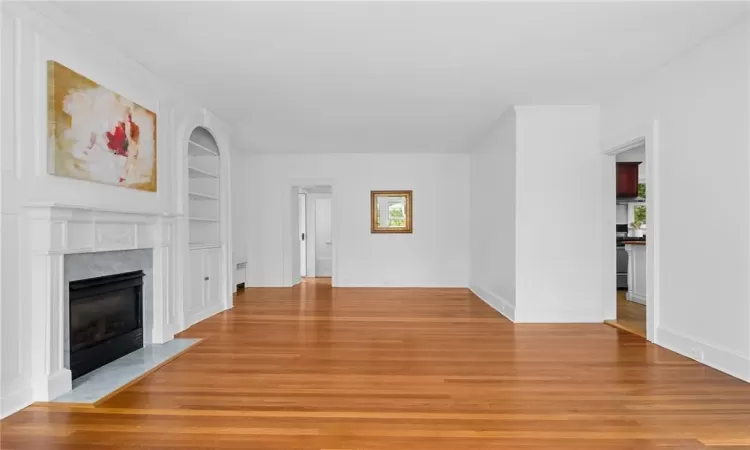 Unfurnished living room featuring a premium fireplace, crown molding, built in shelves, and light hardwood / wood-style flooring