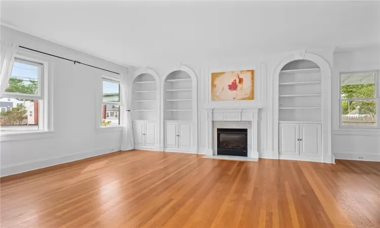 Unfurnished living room with built in shelves and hardwood / wood-style floors