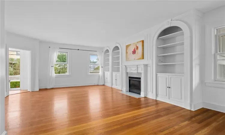 Unfurnished living room featuring light wood-type flooring, a fireplace, and built in shelves