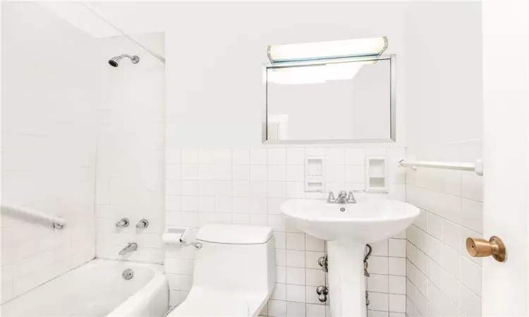 Bathroom featuring tiled shower / bath combo, toilet, decorative backsplash, and tile walls