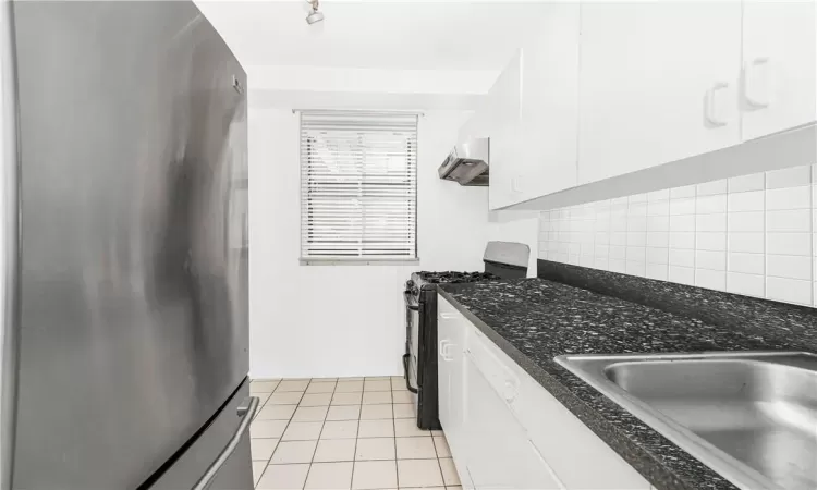 Kitchen featuring wall chimney range hood, decorative backsplash, gas range oven, white cabinetry, and stainless steel fridge