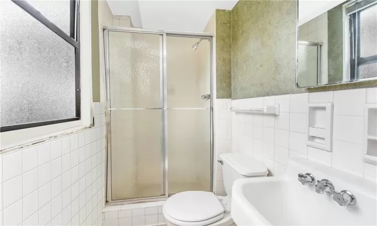 Bathroom featuring tile walls, a shower with shower door, sink, and toilet