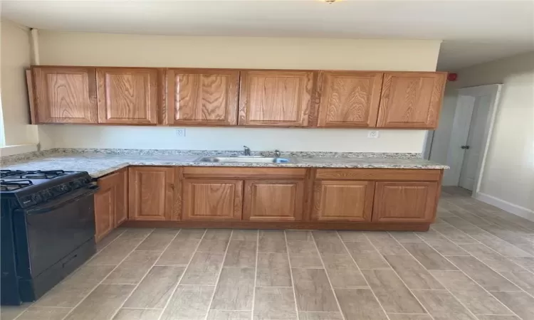 Kitchen with light stone counters, light hardwood / wood-style floors, sink, and black gas range oven