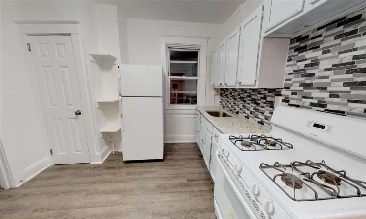 Kitchen featuring white appliances, backsplash, sink, light wood-type flooring, and white cabinets