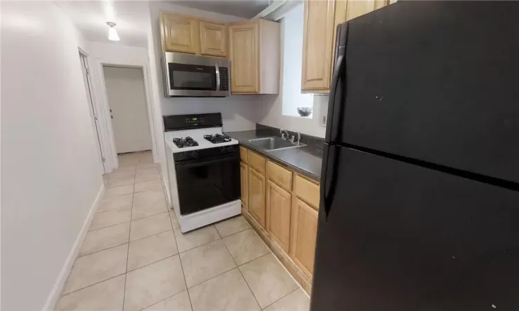 Kitchen with black refrigerator, gas range gas stove, sink, and light tile patterned flooring