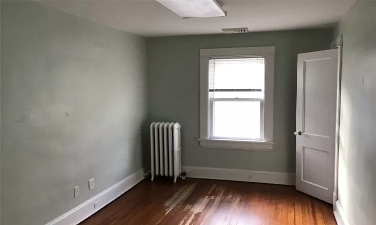 Unfurnished room with radiator heating unit, dark wood-type flooring, and a wealth of natural light