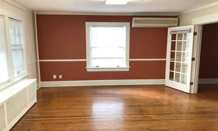 Empty room featuring an AC wall unit, radiator, a wealth of natural light, and dark wood-type flooring